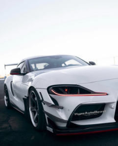 Close up fitment of dry carbon fiber headlight air duct on white Toyota Supra with red LED